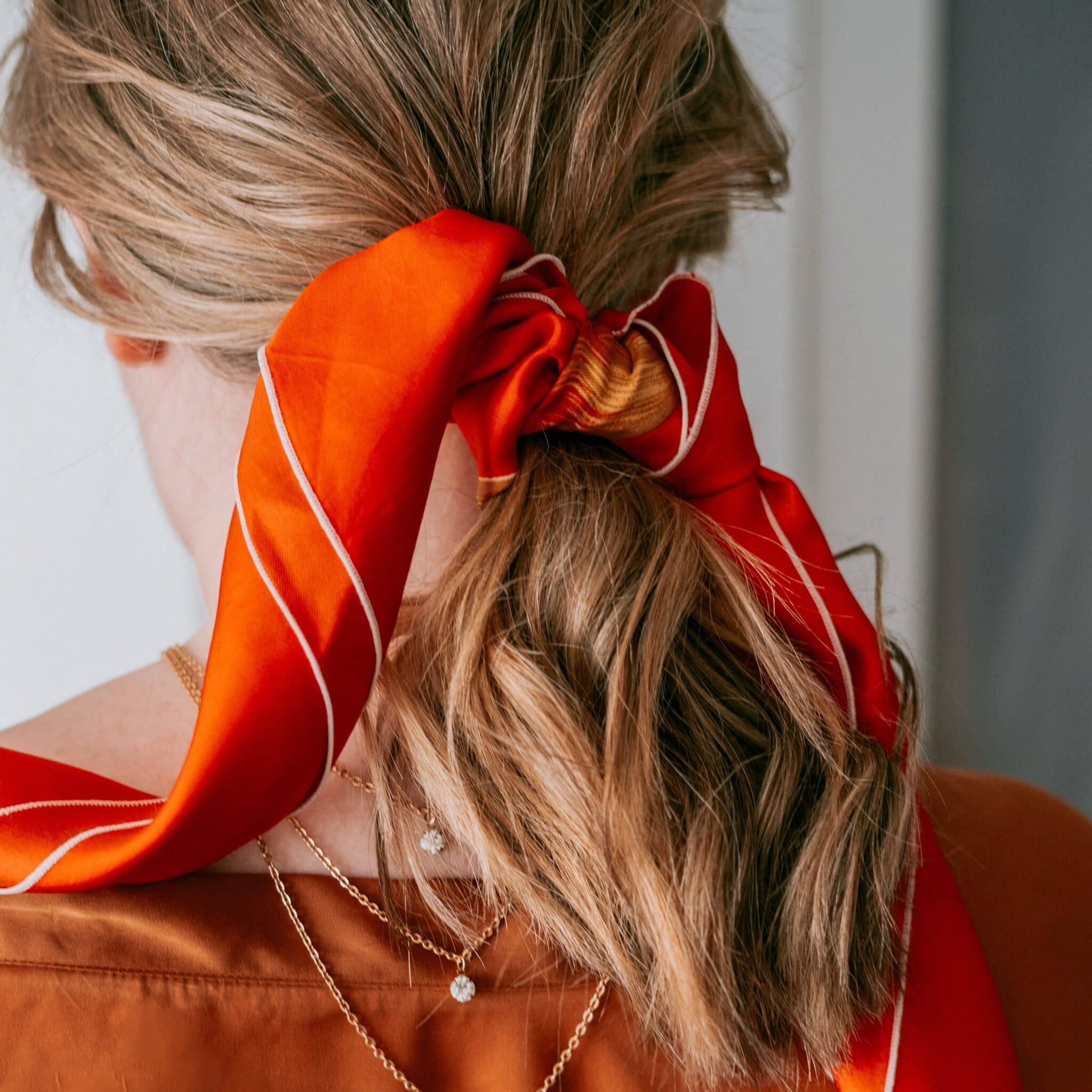 femme blonde de dos qui porte un foulard orange dans les cheveux